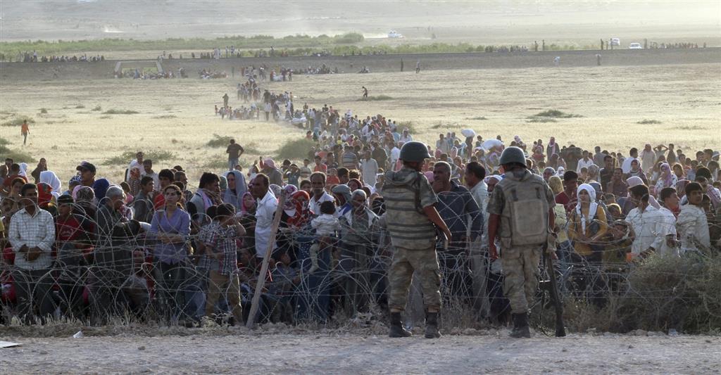 turkish soldiers stand guard syrian refugees wait behind border fences