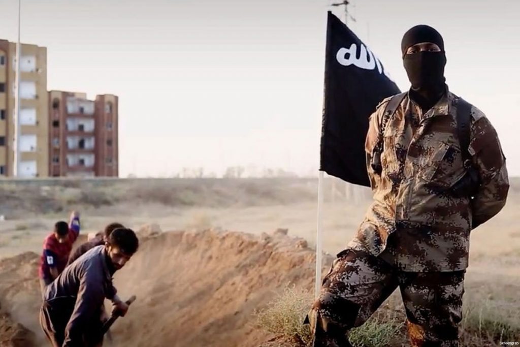 isis soldier posing in front of people digging their own graves