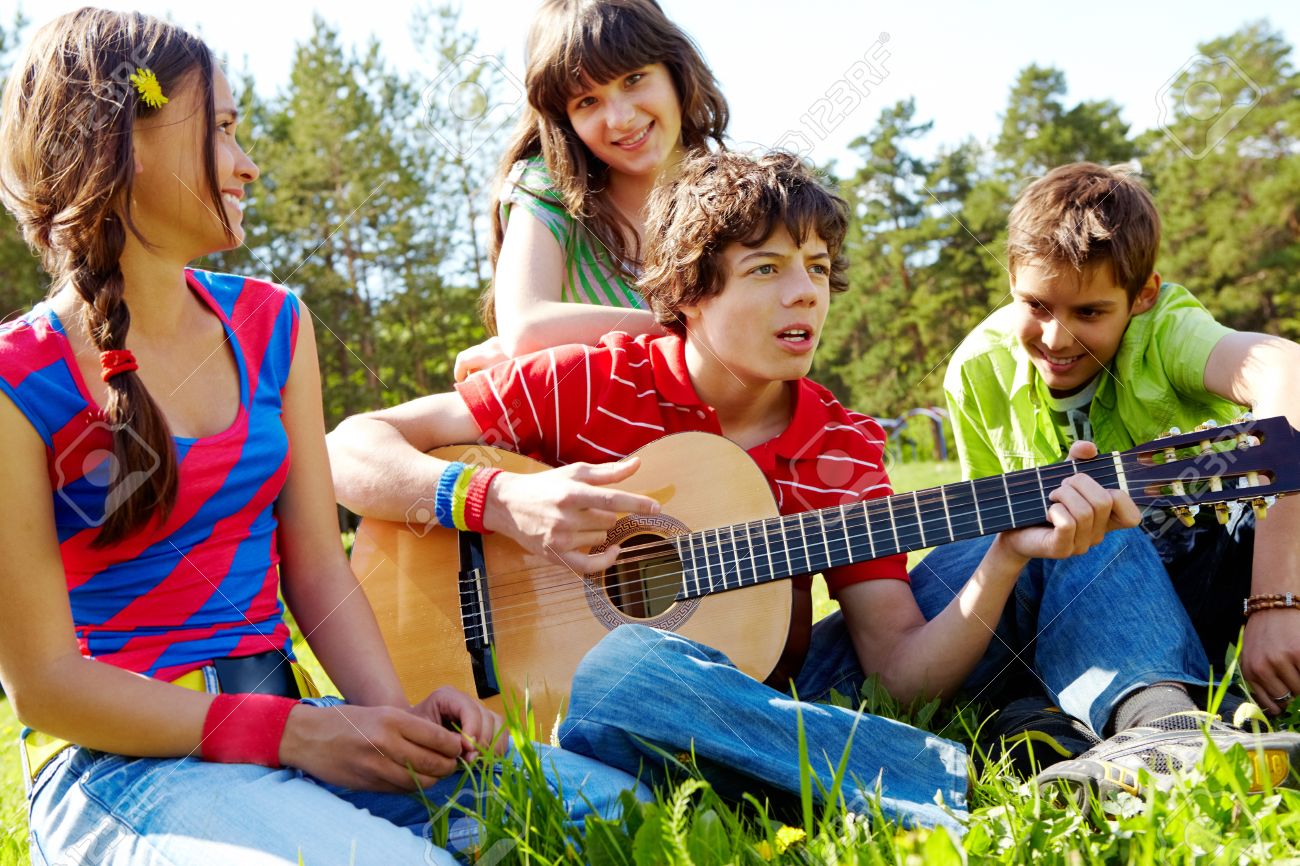 9494621 Portrait of handsome lad playing the guitar surrounded by his friends Stock Photo